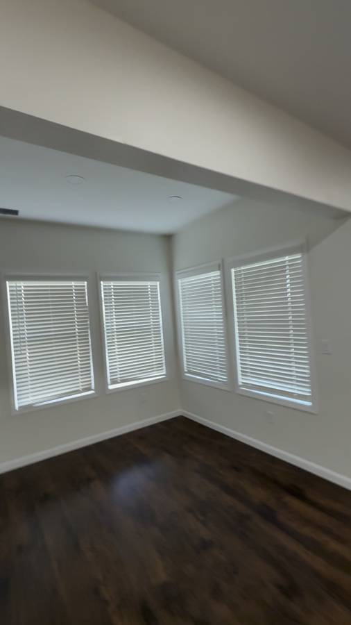 Finished basement bay window room with blinds and dark wood flooring